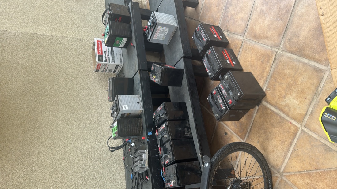 A bench covered in a dozen assorted car batteries