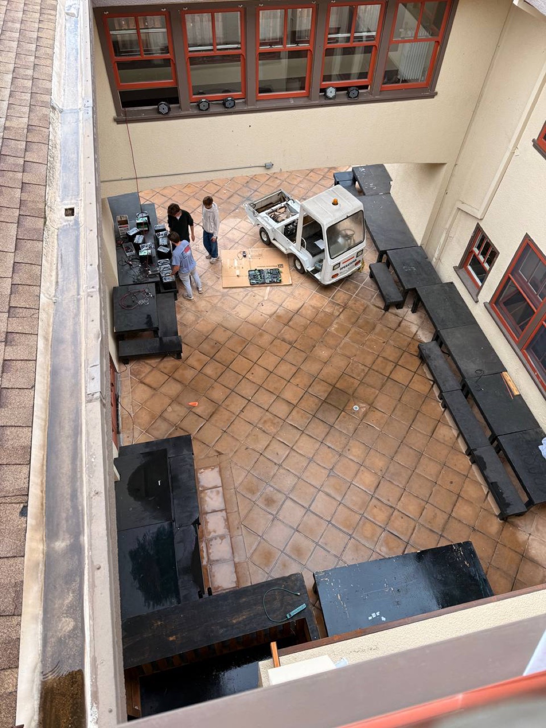 Overhead view of a courtyard with the truck's hood open and three people working on it, parts laid out on the ground