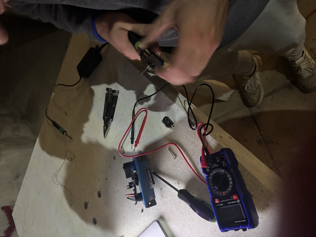 A workbench at night with a multimeter, screwdriver, and the disassembled accelerator pedal mid-repair