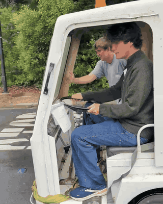 One person steering the Taylor-Dunn while another pushes it down the road